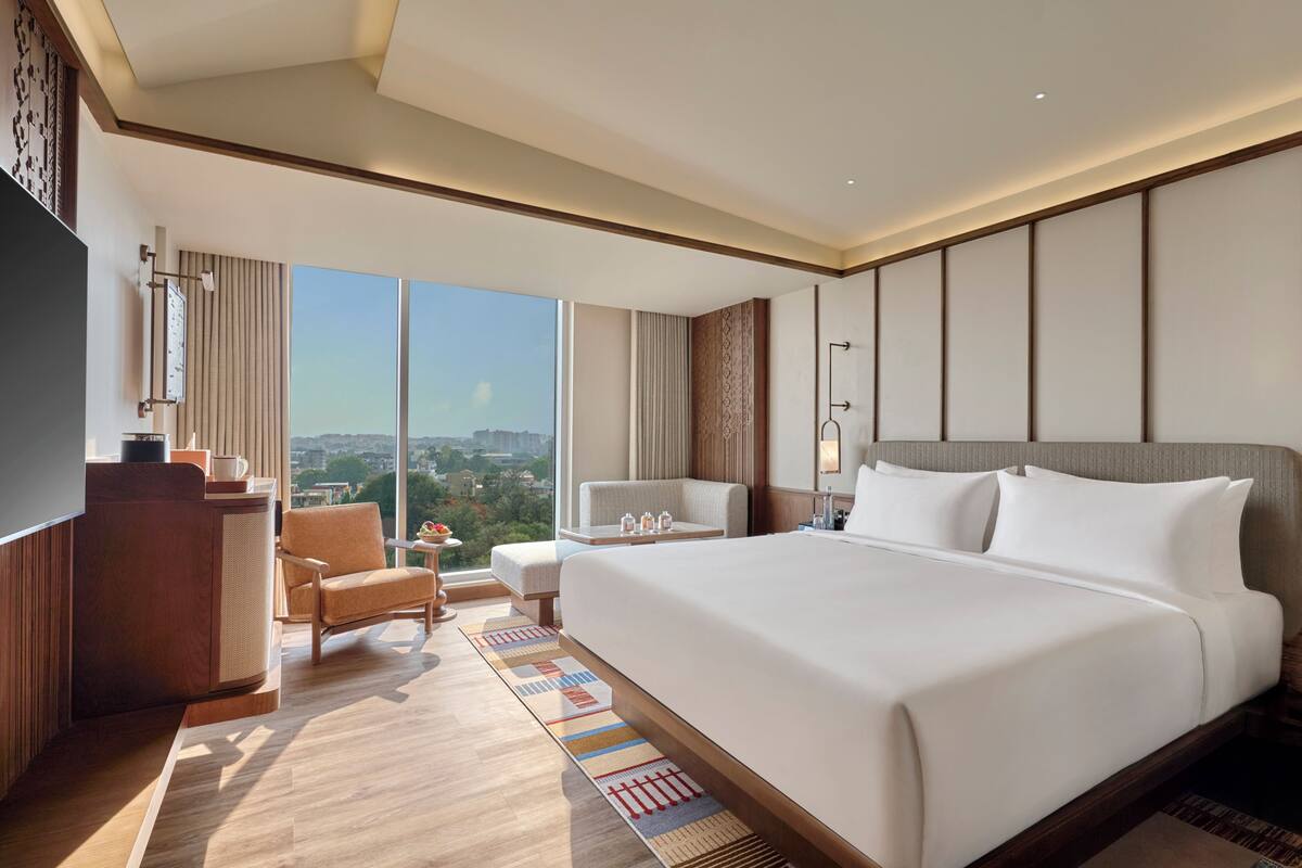 A hotel room with a large bed, a desk, a chair, a TV, and a view of the city.