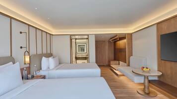 A hotel room with two beds, a small table with fruit, a sofa, and a TV.