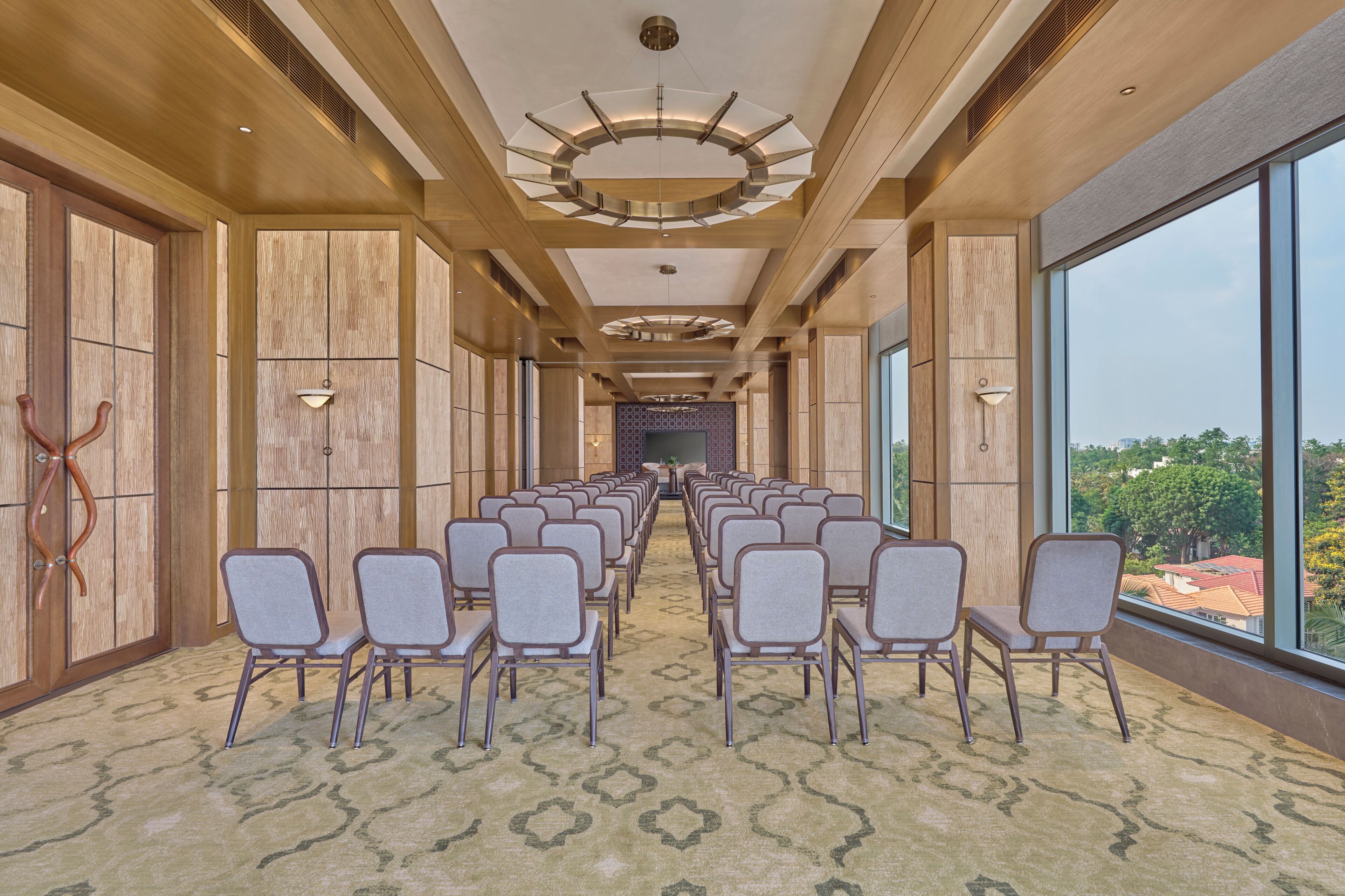 Une salle de conférence avec des rangées de chaises, de grandes fenêtres et un tapis à motifs.