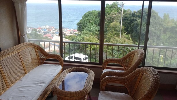 A balcony with wicker furniture, a view of the sea, and a building in the background.