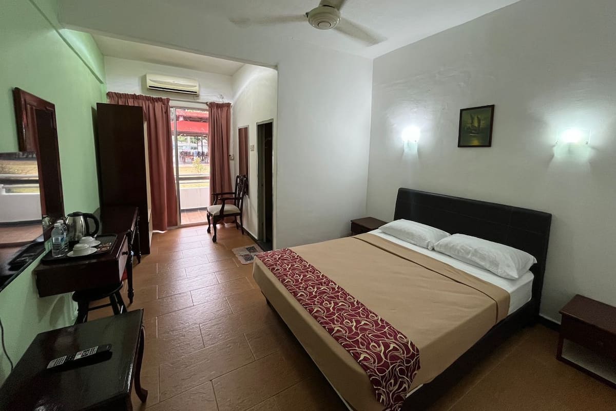 Una habitación de hotel con cama, escritorio y silla, mesa y silla, ventilador de techo y ventana con cortinas.
