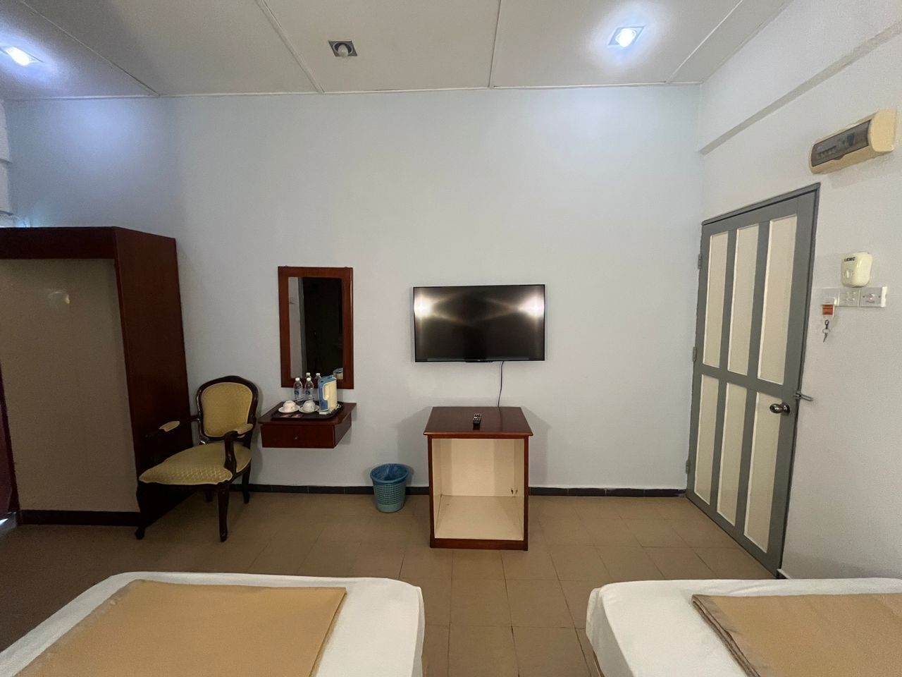 Habitación de hotel con dos camas, un televisor, una mesita de madera, una silla, un espejo y una puerta.