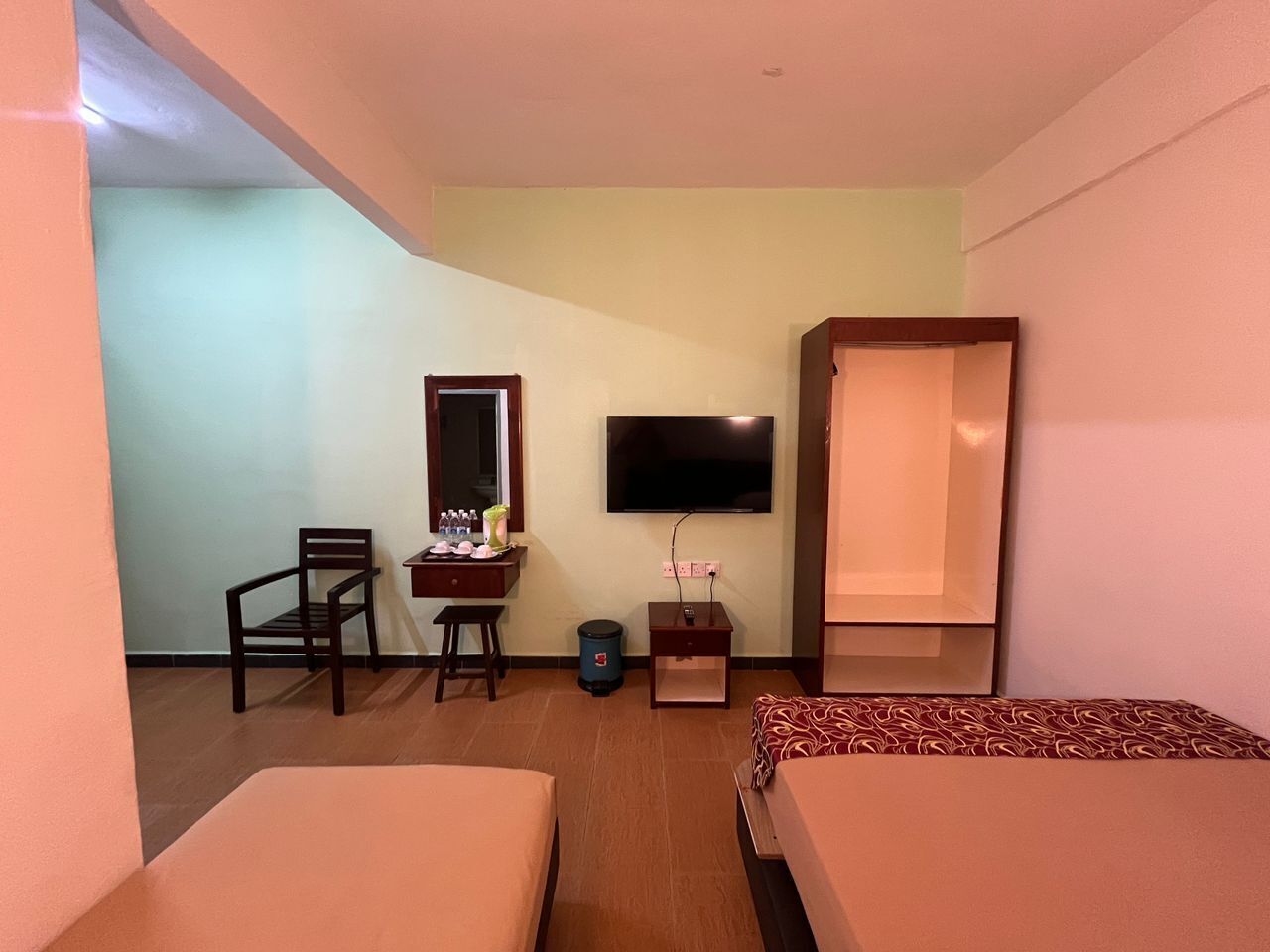 Habitación de hotel con dos camas, un escritorio con silla, un televisor y una pequeña mesa con un florero.