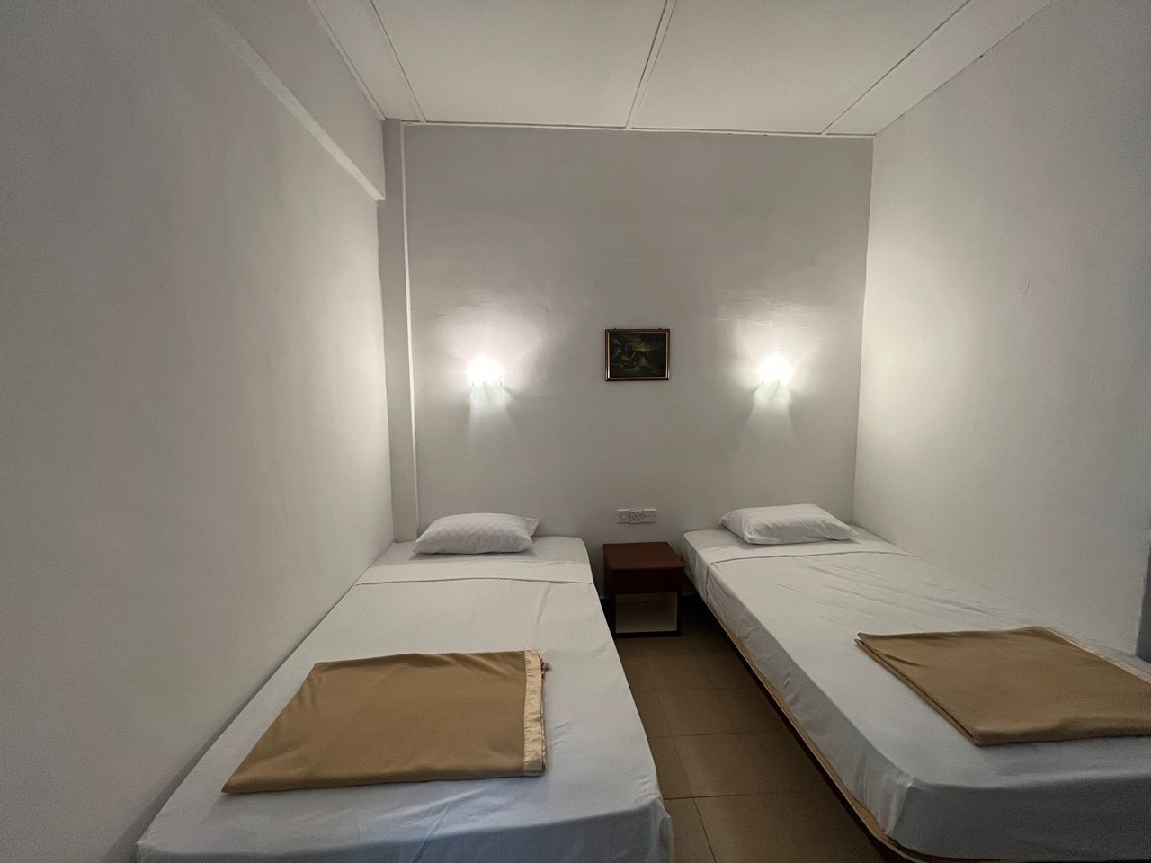A small, clean room with two single beds, a nightstand, and two wall-mounted lights.