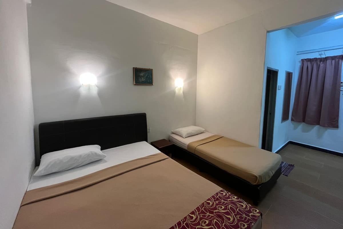 Una habitación con dos camas, una mesita de noche, una lámpara de pared y una puerta que da a otra estancia.
