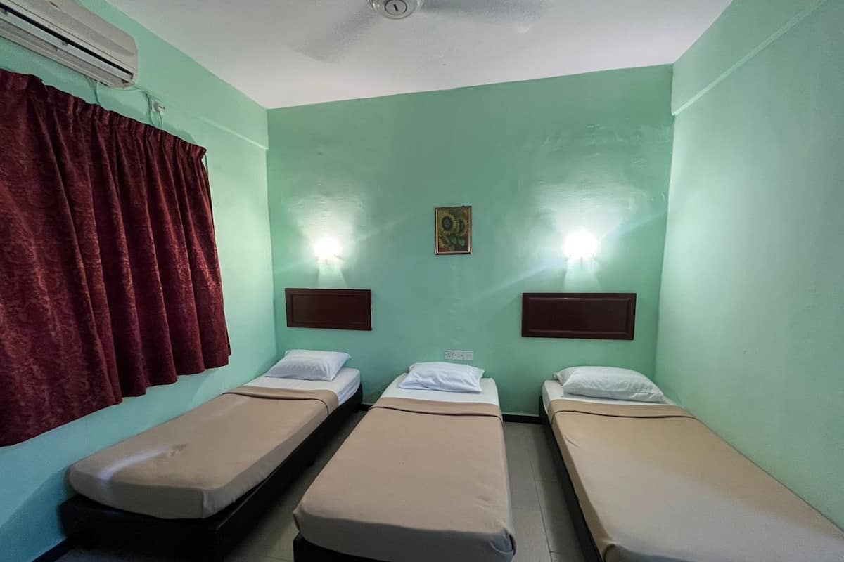 Una habitación con tres camas individuales, una cortina roja, un equipo de aire acondicionado y dos lámparas fijadas a la pared.