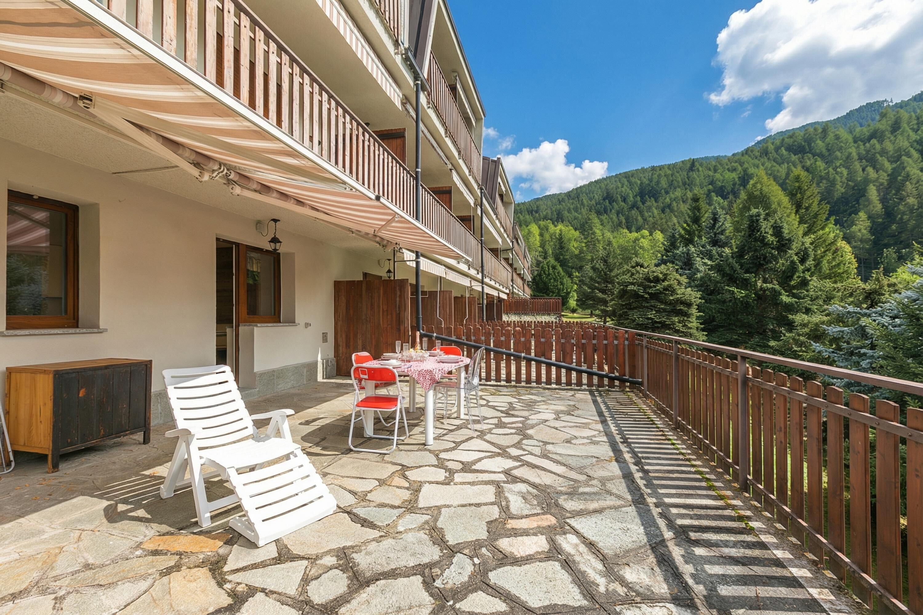 A balcony with stone flooring, white chairs, and a table with a red and white tablecloth.