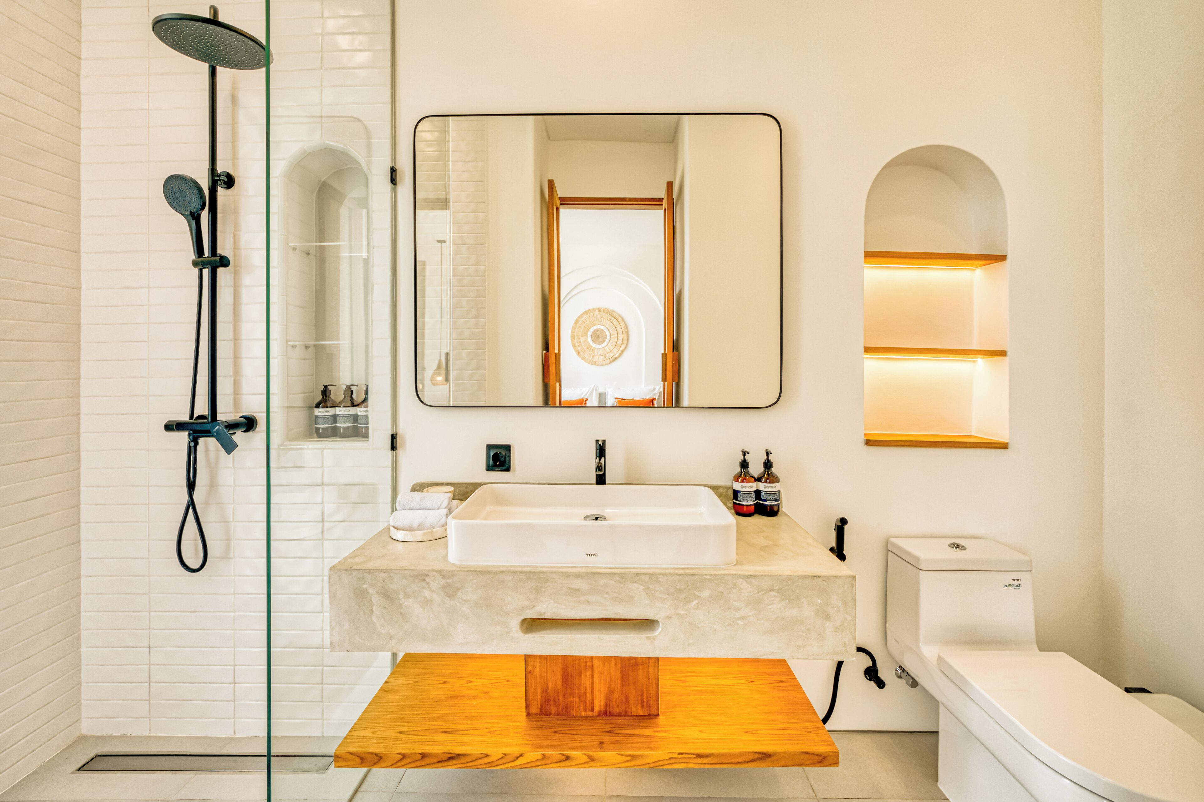 A modern bathroom with a large mirror, a shower, a sink, and a toilet.