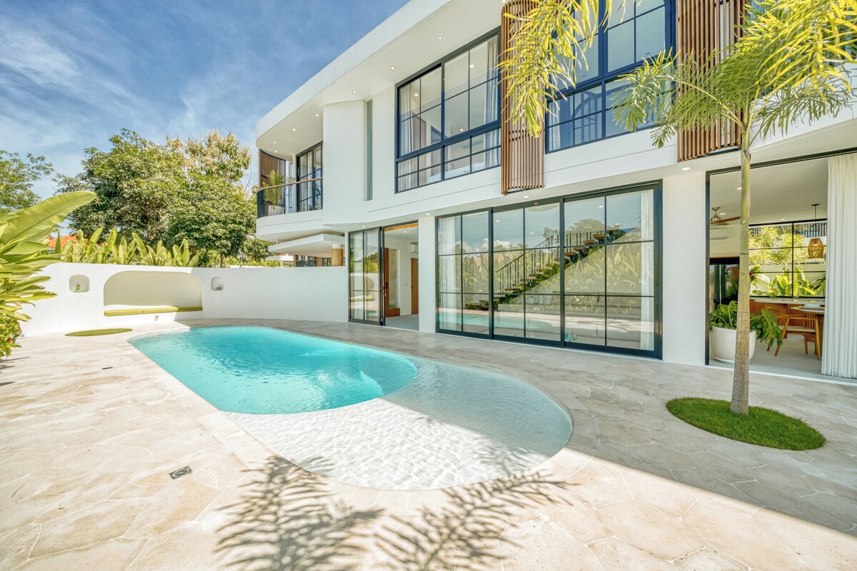 A modern two-story house with a swimming pool, large windows, and a staircase leading to the upper floor.