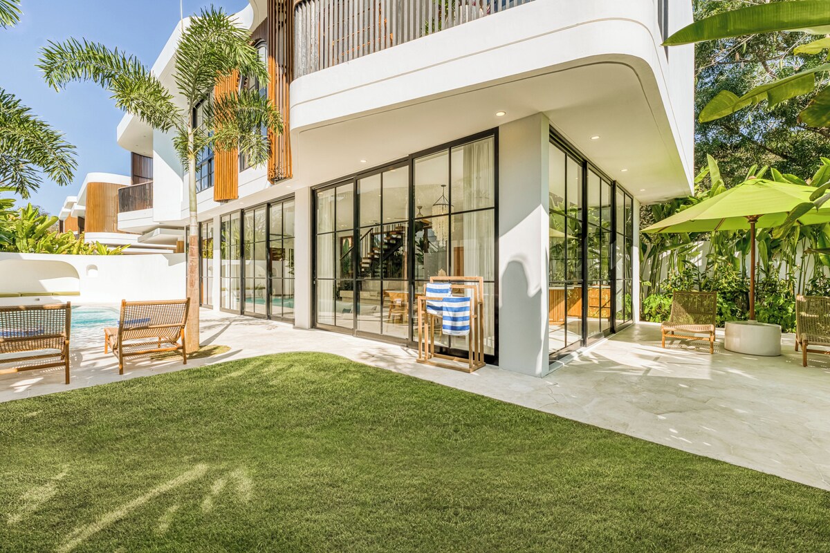 A modern house with a glass-enclosed patio, outdoor furniture, and a well-maintained lawn.
