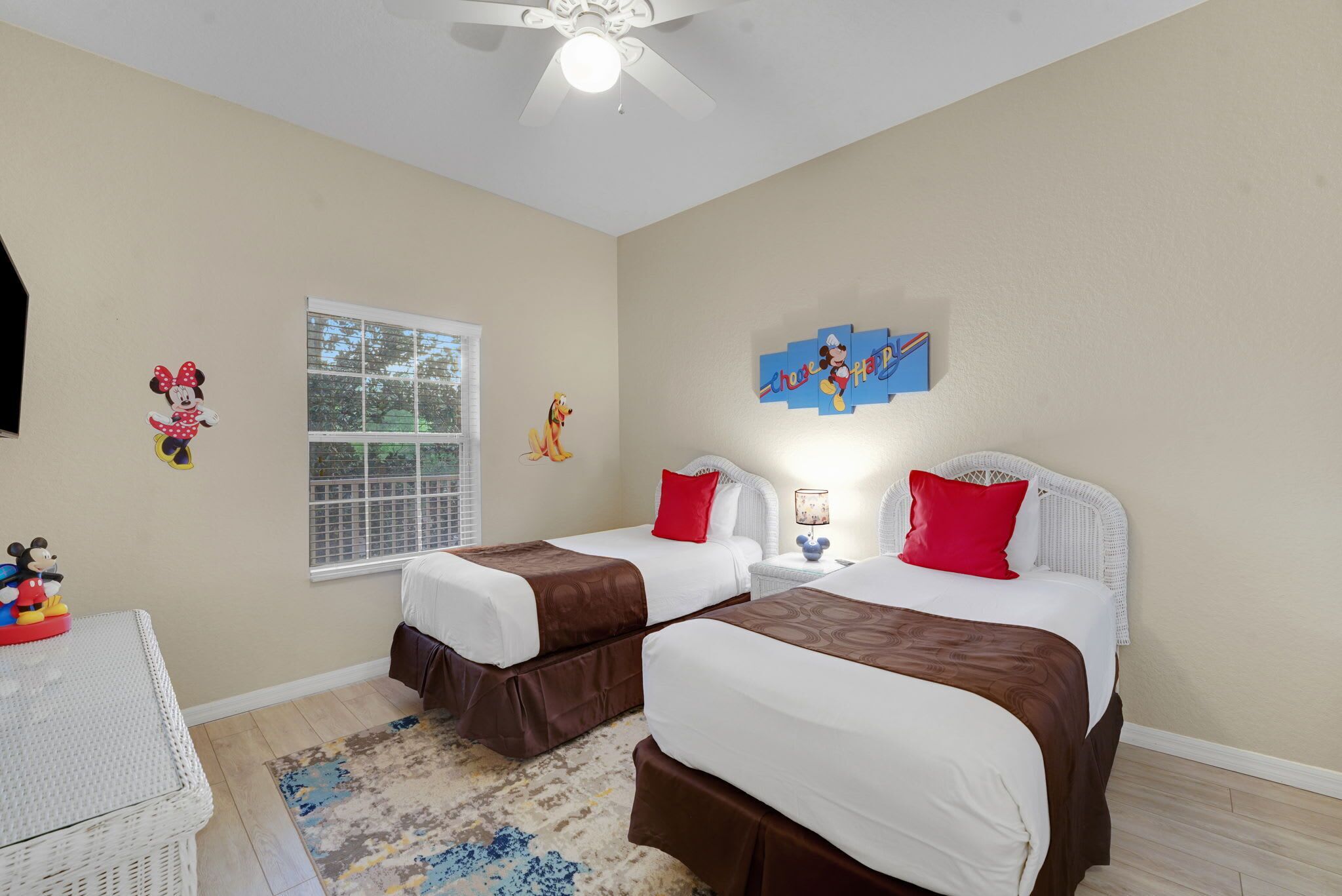 A hotel room with two beds, a ceiling fan, a window, and wall decorations including Mickey Mouse and a Disney theme.