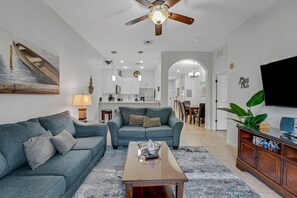 A living room with two sofas, a coffee table, a TV, and a ceiling fan. - Exclusive villa: pool, EV charger, near Disney (Davenport)