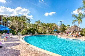 A swimming pool with lounge chairs and umbrellas, surrounded by palm trees and a thatched-roof hut. - 2nd floor condo near theme parks, balcony, pools, restaurant, basketball court (Davenport)
