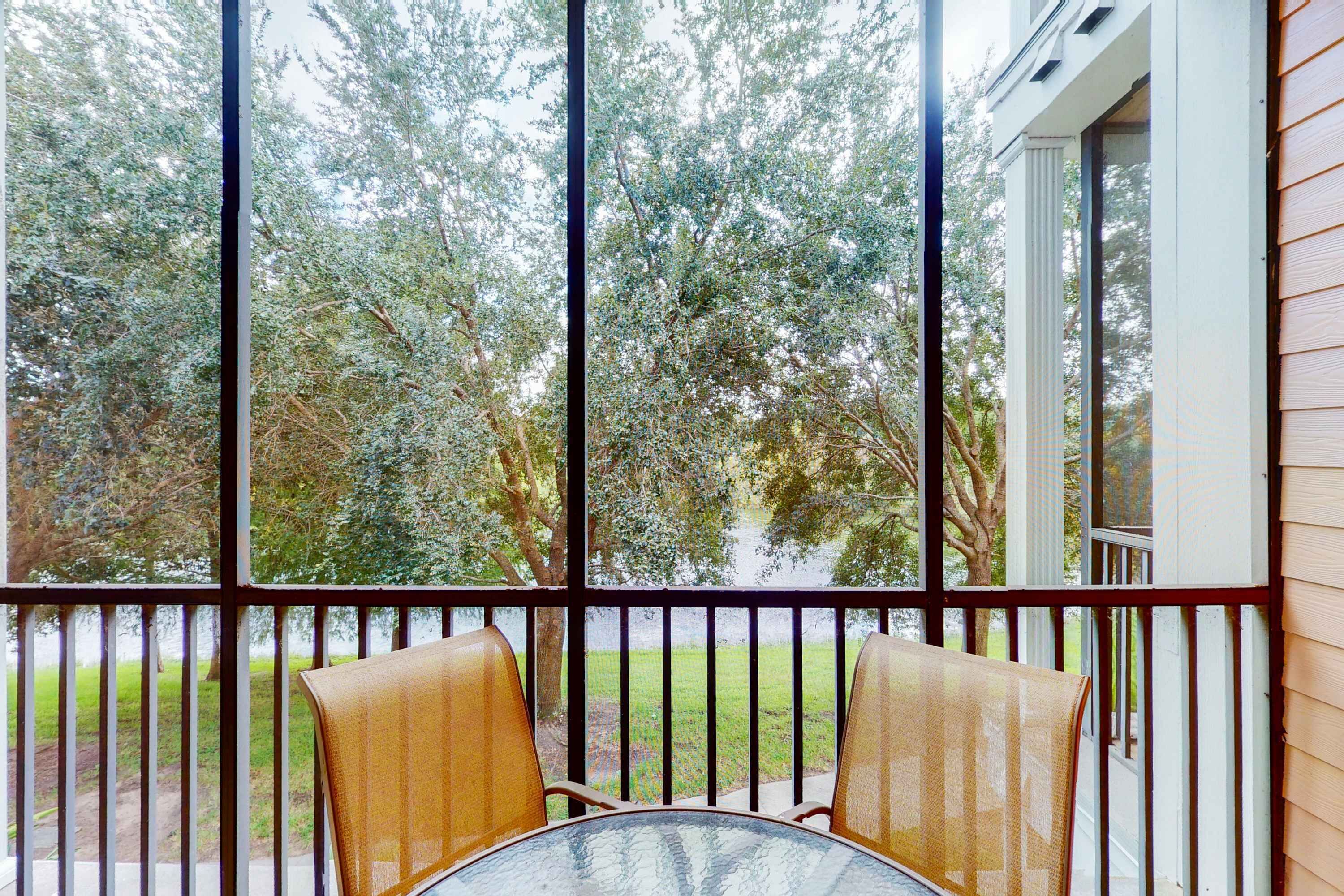 Balcón con dos sillas y una mesa, con vista a una zona verde con árboles.