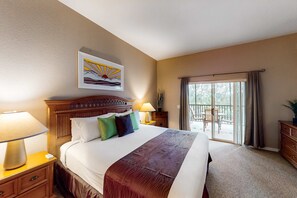 A hotel room with a large bed, a wooden headboard, a painting above the bed, a nightstand with a lamp, a dresser, and a view of the outside through a sliding glass door. - Snowbird-friendly resort condo with private balcony, pool & hot tub - near parks (Davenport)