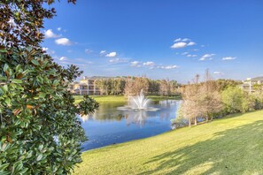 Ein friedlicher Park mit Teich, Springbrunnen und Gebäuden im Hintergrund.