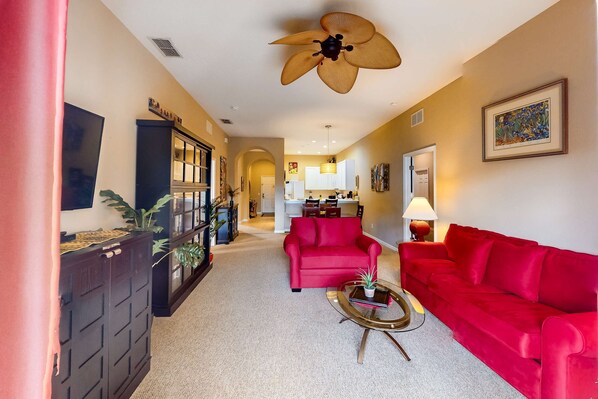 A spacious living room with a red sofa, a coffee table, and a ceiling fan. - Snowbird-friendly resort condo with private balcony, pool & hot tub - near parks (Davenport)