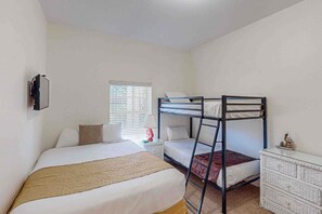 Ein Schlafzimmer mit Etagenbett, einem Einzelbett, einem Schminktisch, einem Nachttisch und einem Fenster mit Jalousien.