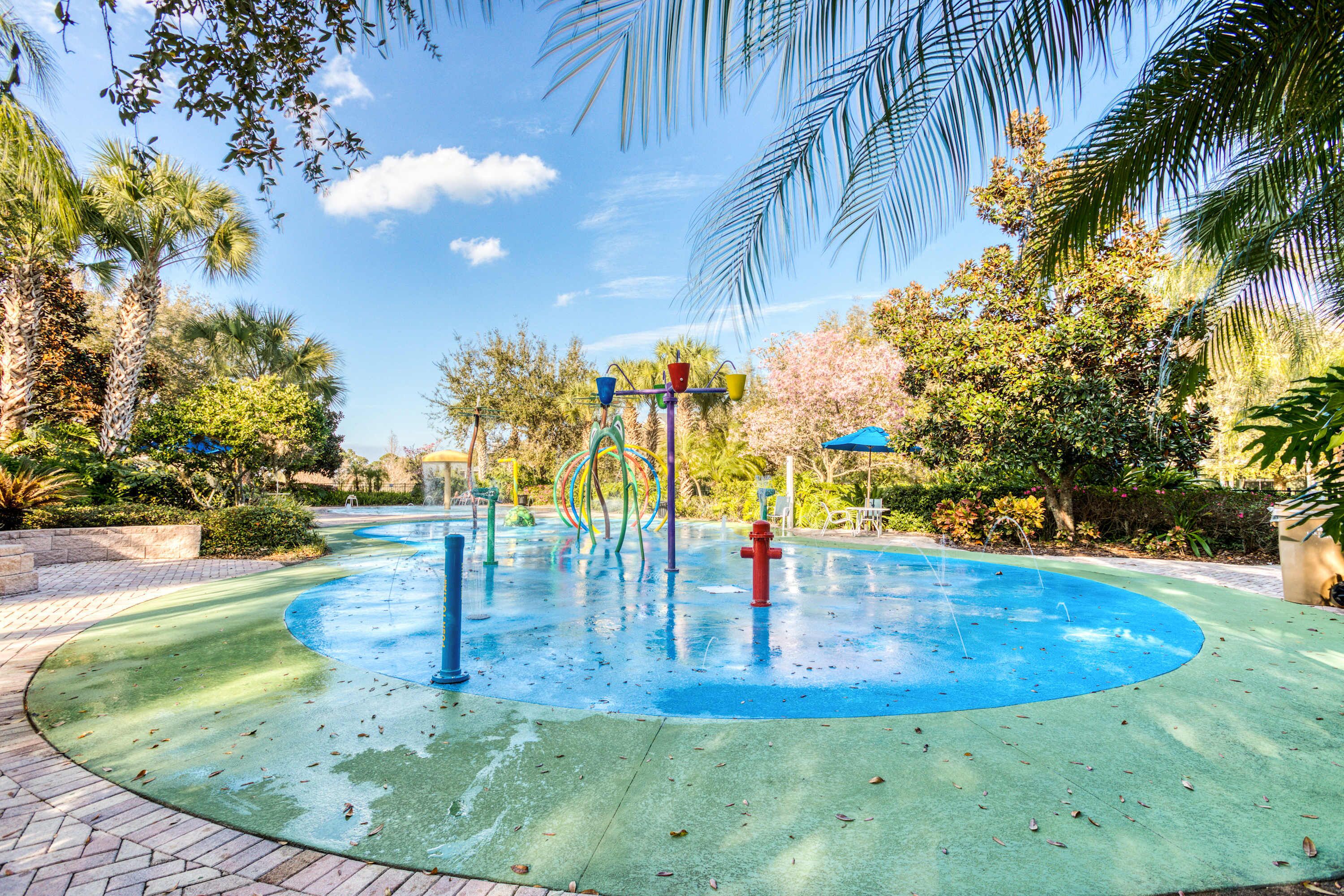 A water play area with a circular pool, surrounded by palm trees and greenery.