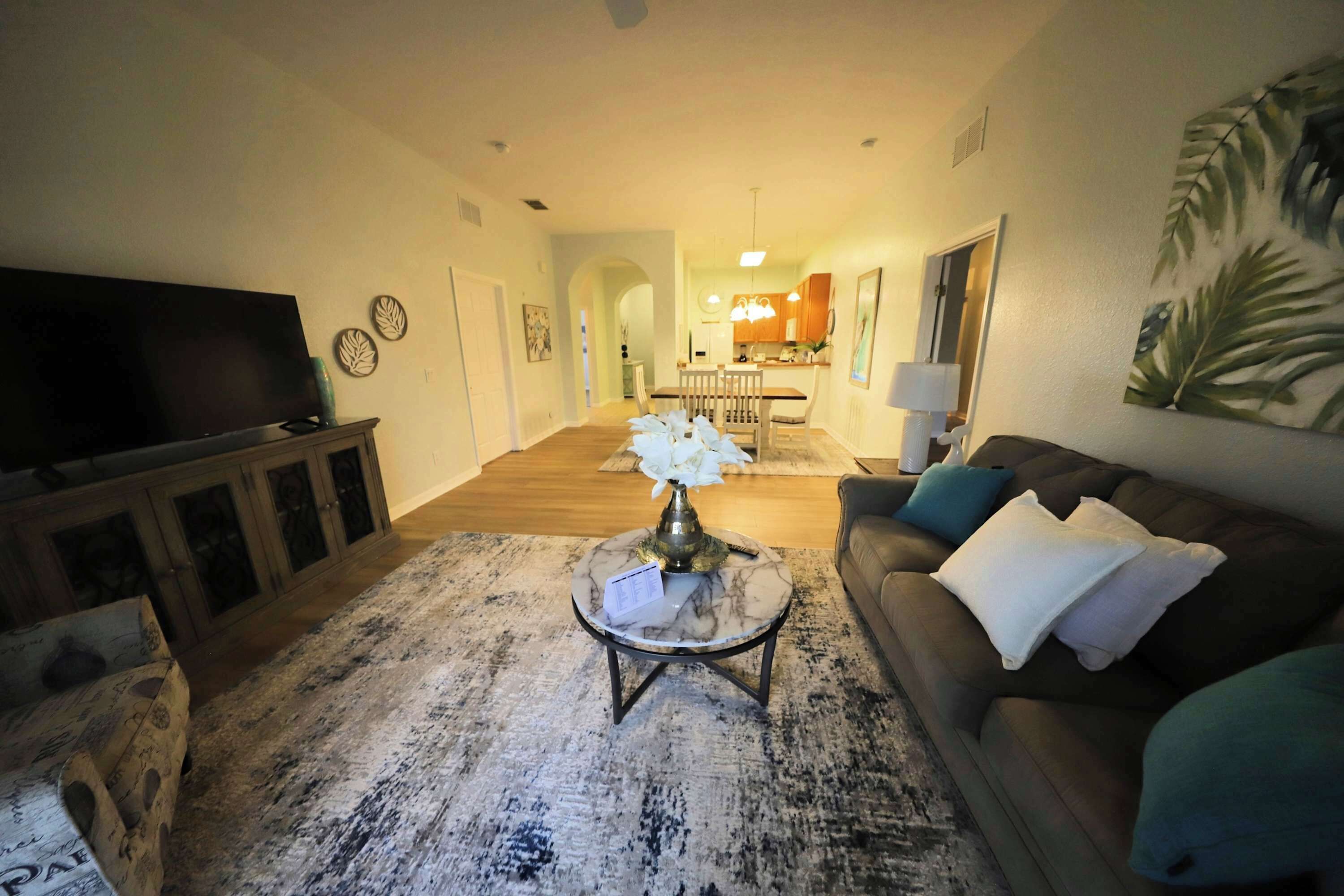 Ein Wohnzimmer mit Flachbildfernseher, Couchtisch mit Vase, Sofa mit Kissen und einem großen Gemälde an der Wand.