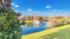 A serene outdoor setting with a pond, a fountain, and a well-maintained lawn. - 1st floor condo w/ basketball court, gym, sauna, shared pools, near theme parks (Davenport)