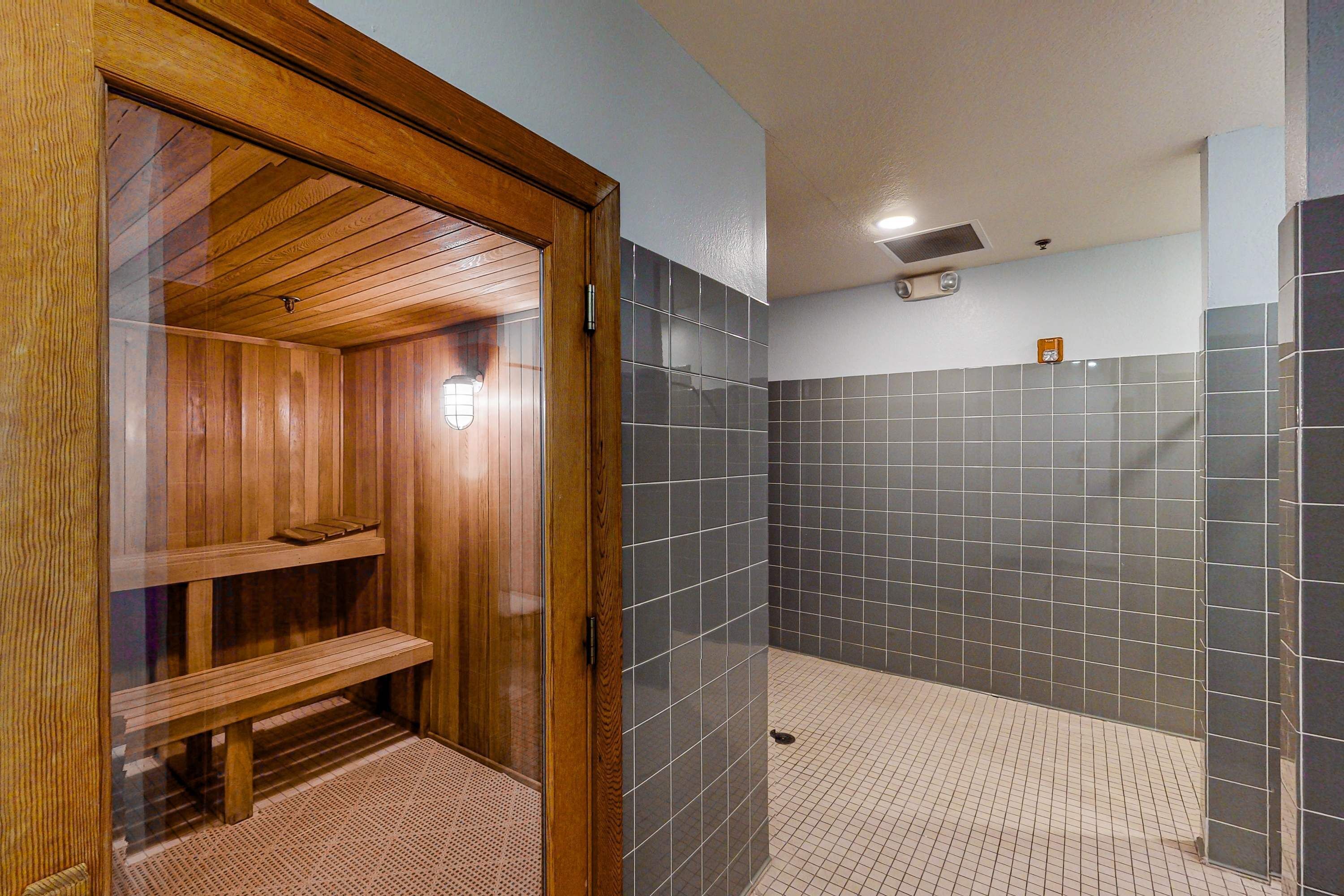 Una sauna con bancos de madera y zona de ducha revestida con azulejos.