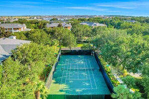 Ein Luftbild zeigt einen Tennisplatz, der von üppigem Grün und Wohnhäusern umgeben ist.