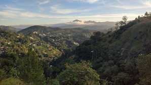 A panoramic view of a hilly landscape with scattered buildings, likely a resort or hotel area, surrounded by dense greenery and mountains in the distance. - Ella T & D Resort (Ella)