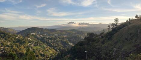 A panoramic view of a hilly landscape with scattered buildings, likely a resort or hotel area, surrounded by dense greenery and mountains in the distance.