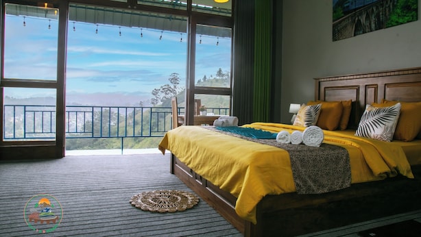 A bedroom with a large bed, a view of the outdoors, and a wooden floor. - Ella T & D Resort (Ella)