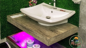 A bathroom with a marble wall, a green artificial grass floor, a white sink, a mirror, and a hairdryer on the wall. - Ella T & D Resort (Ella)