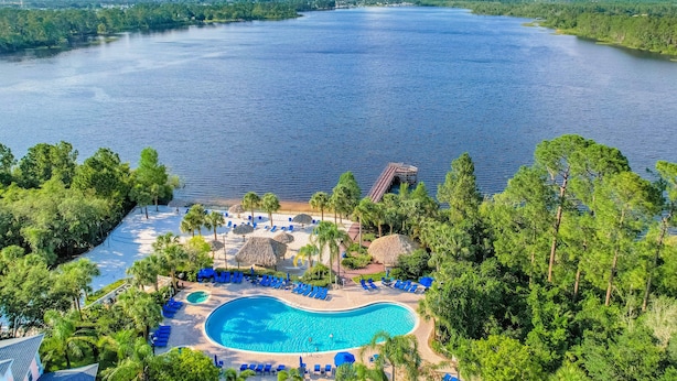 Ein Resort mit einem großen Schwimmbecken, umgeben von Palmen und Liegestühlen, mit Blick auf ein großes Gewässer.