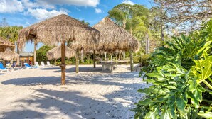Una playa con sombrillas de paja, sillas de descanso y una zona de arena.