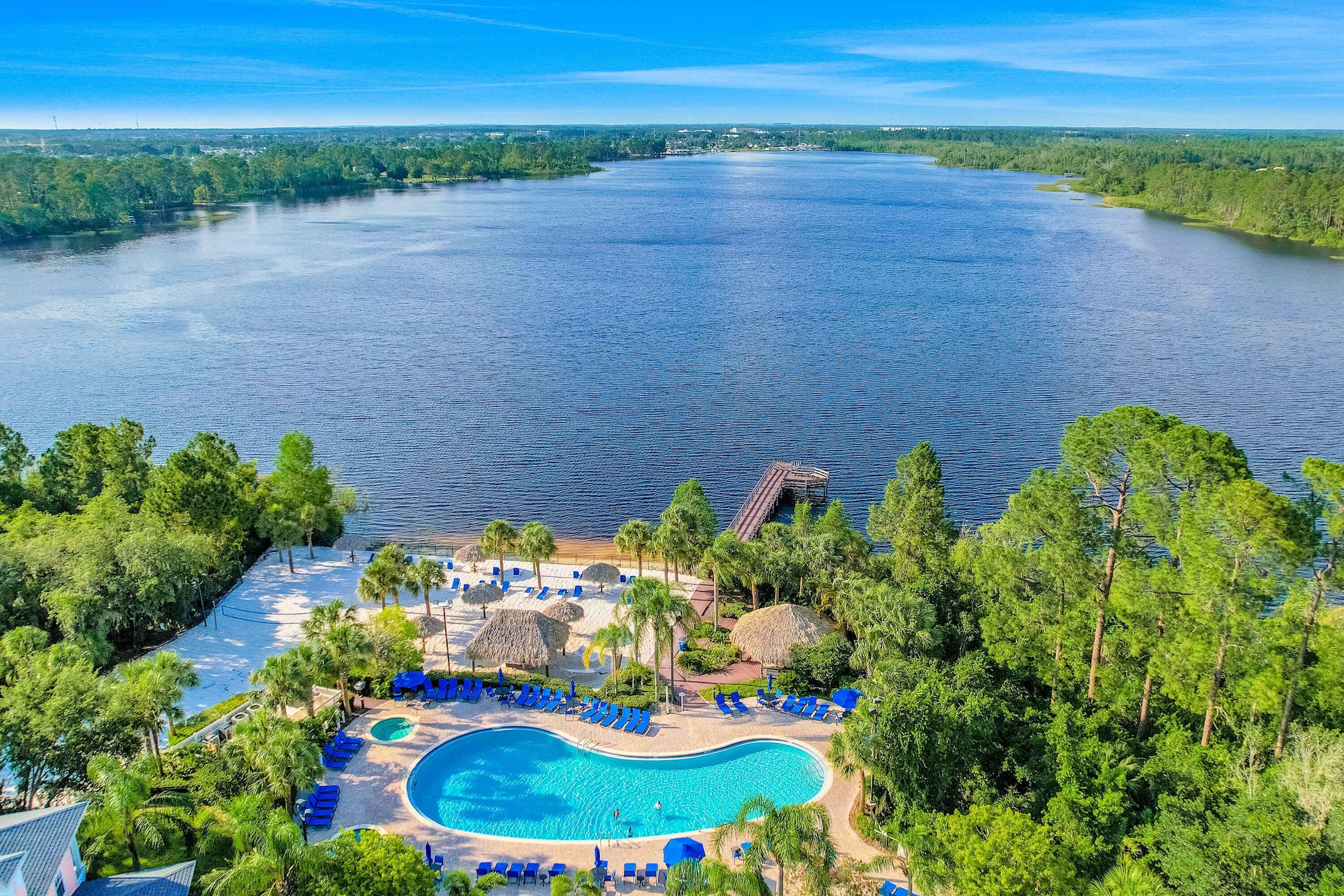 A resort with a large swimming pool surrounded by palm trees and lounge chairs, overlooking a large body of water.
