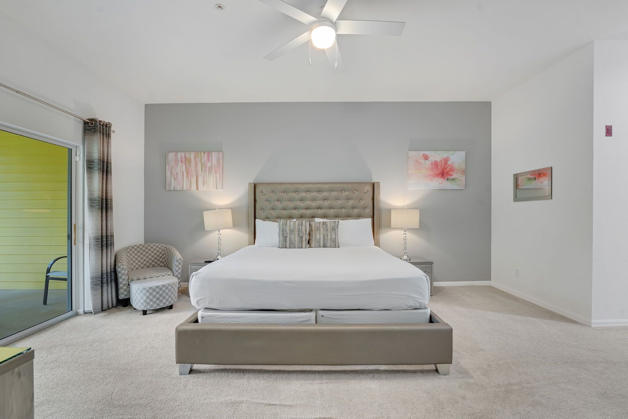 A bedroom with a large bed, two bedside tables with lamps, a chair, and a ceiling fan.