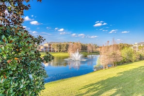 Ein friedlicher Park mit Teich, Springbrunnen und Gebäuden im Hintergrund.