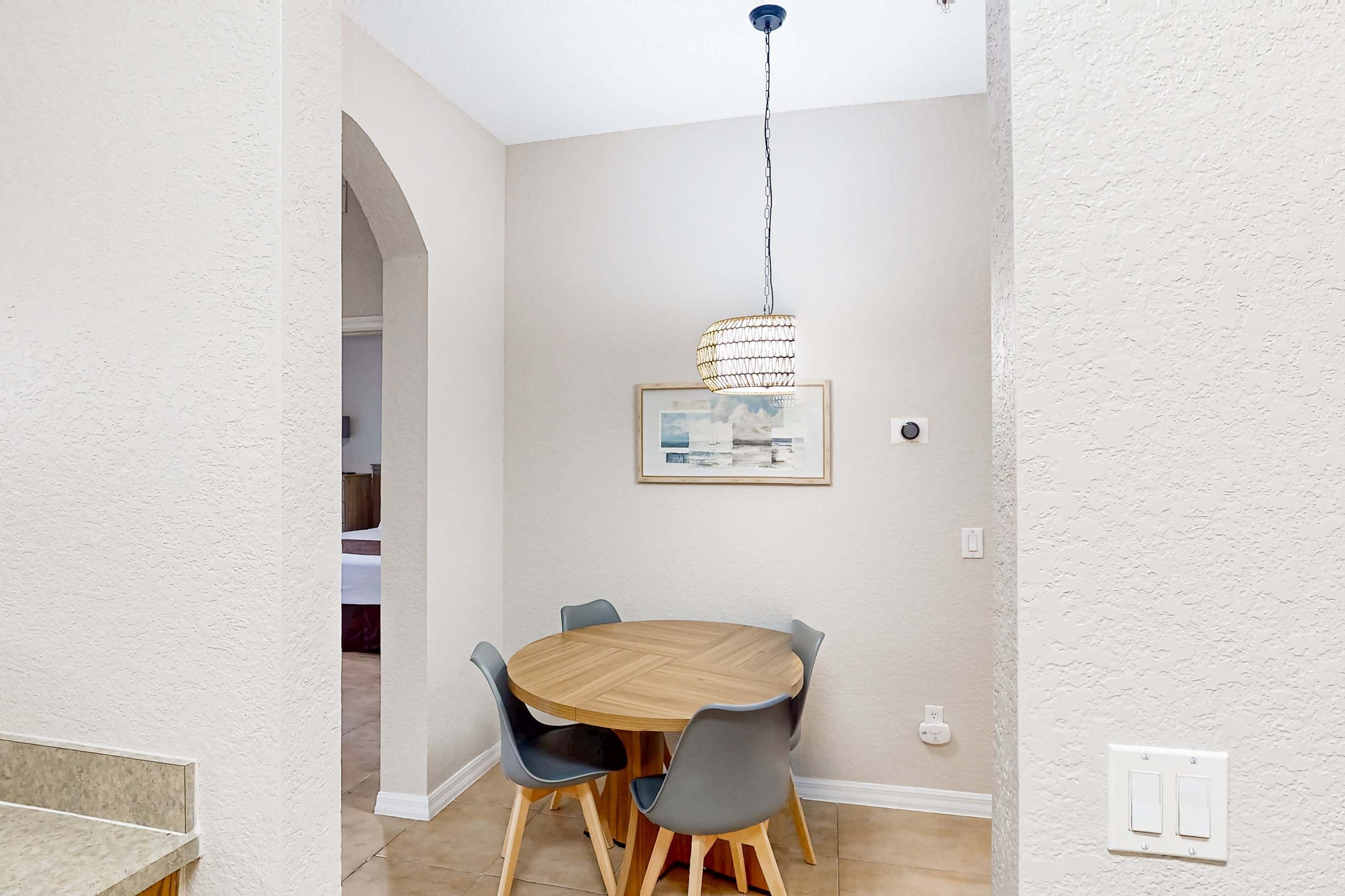 Ein Essbereich mit einem runden Holztisch, vier Stühlen, einer Hängeleuchte und einem gerahmten Bild an der Wand.