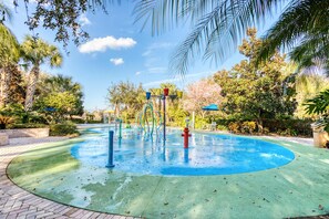 Ein Wasserspielbereich mit einem runden Pool, umgeben von Palmen und Grünpflanzen.