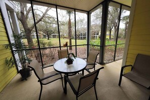 A covered patio with a round table and four chairs, overlooking a landscaped garden with trees and a lawn. - 1st floor condo near theme parks, sauna, tennis court, basketball court, patio (Davenport)