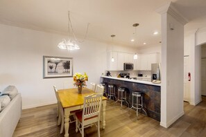 A modern kitchen with white cabinets, a wooden dining table, and bar stools. - 2nd-Floor Comfortable Condo w/ Shared Pools, Hot Tub, High-Speed WiFi, & A/C (Davenport)