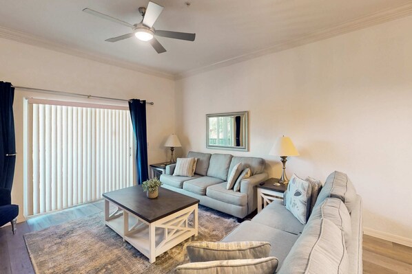 A living room with a sofa, a coffee table, a lamp, and a ceiling fan. - 2nd-Floor Comfortable Condo w/ Shared Pools, Hot Tub, High-Speed WiFi, & A/C (Davenport)