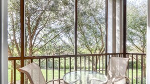 Ein Balkon mit einem Glastisch und zwei Stühlen, mit Blick auf einen Garten mit Bäumen.
