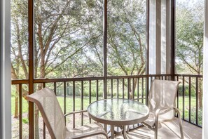 A balcony with a glass table and two chairs, overlooking a garden with trees. - Ground-Floor Condo near Theme Parks w/Shared Pools, Hot Tub, Gym, Sport Courts (Davenport)