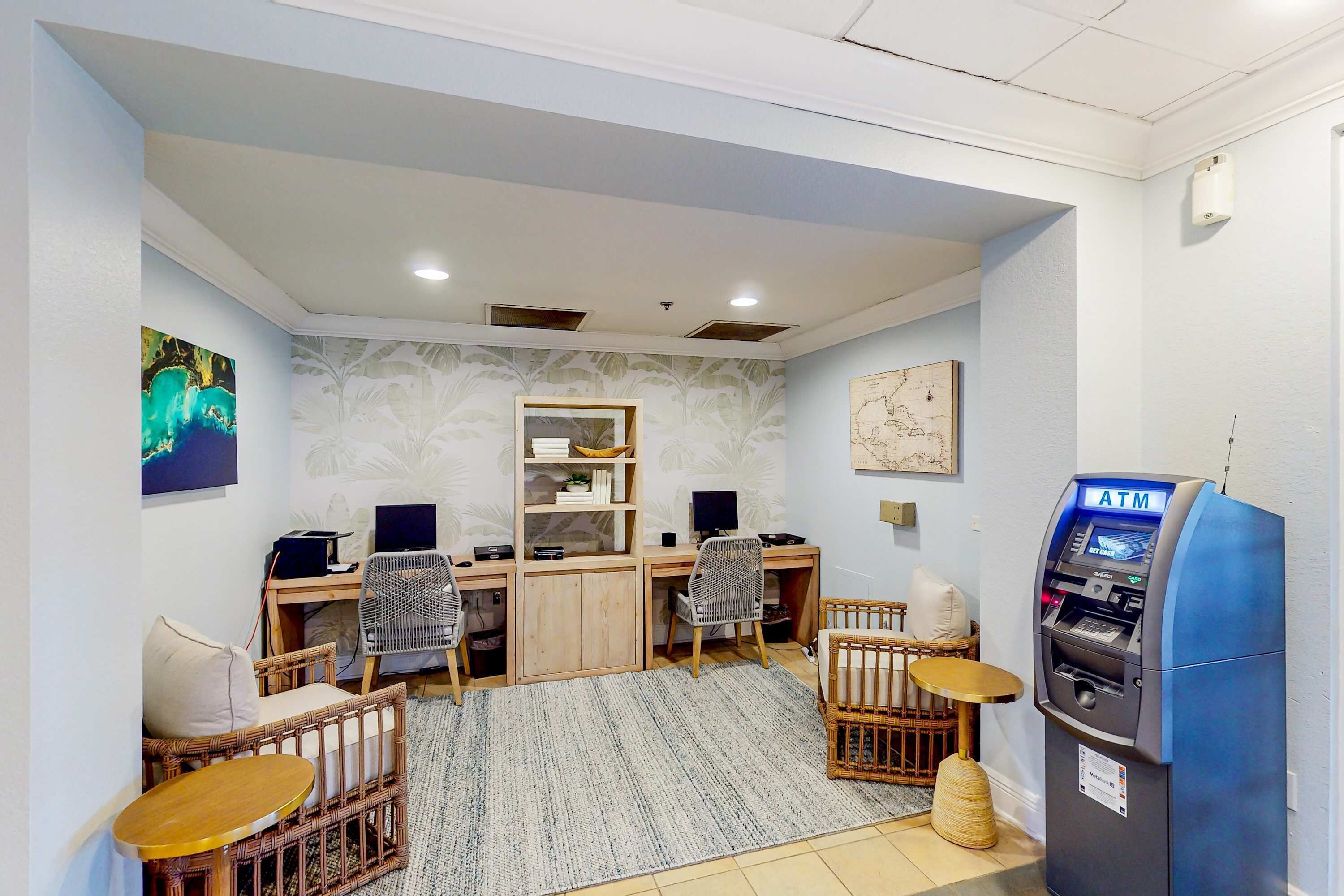 A room with a desk, two chairs, a small table, a crib, and an ATM.