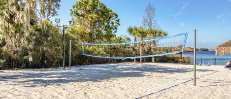 En strandvolleyballbane med net, omgivet af sand og træer.