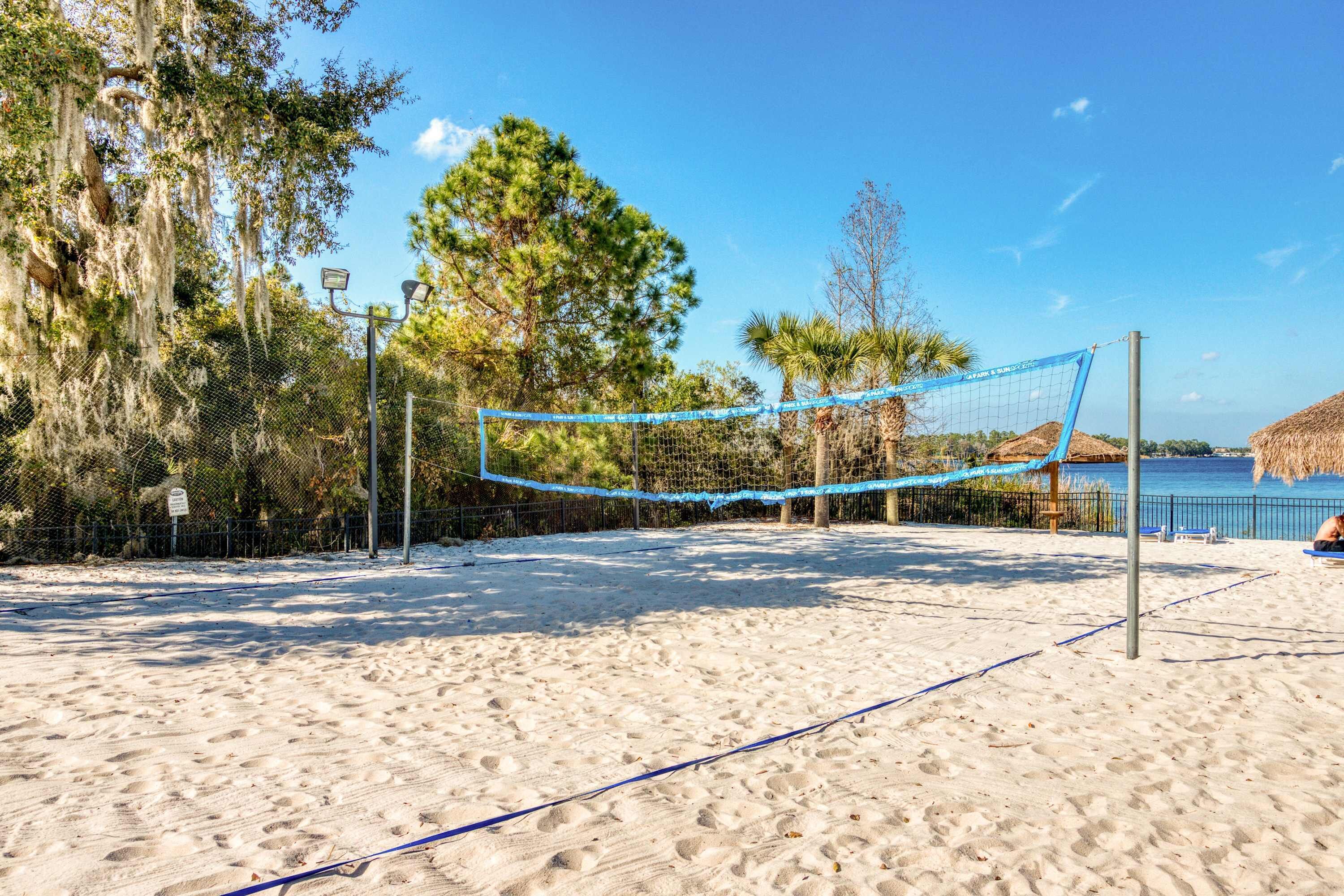 A beach volleyball court with a net, surrounded by sand and trees.
