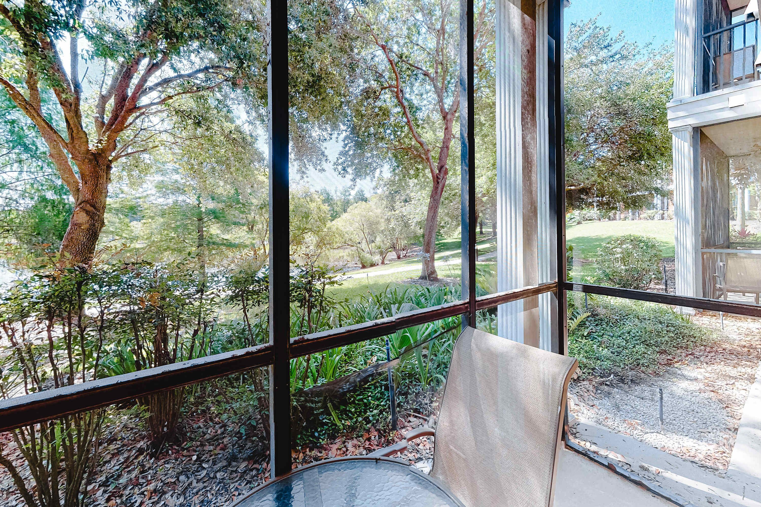 Quarto com grandes janelas, oferecendo vista para um jardim com árvores e gramado.