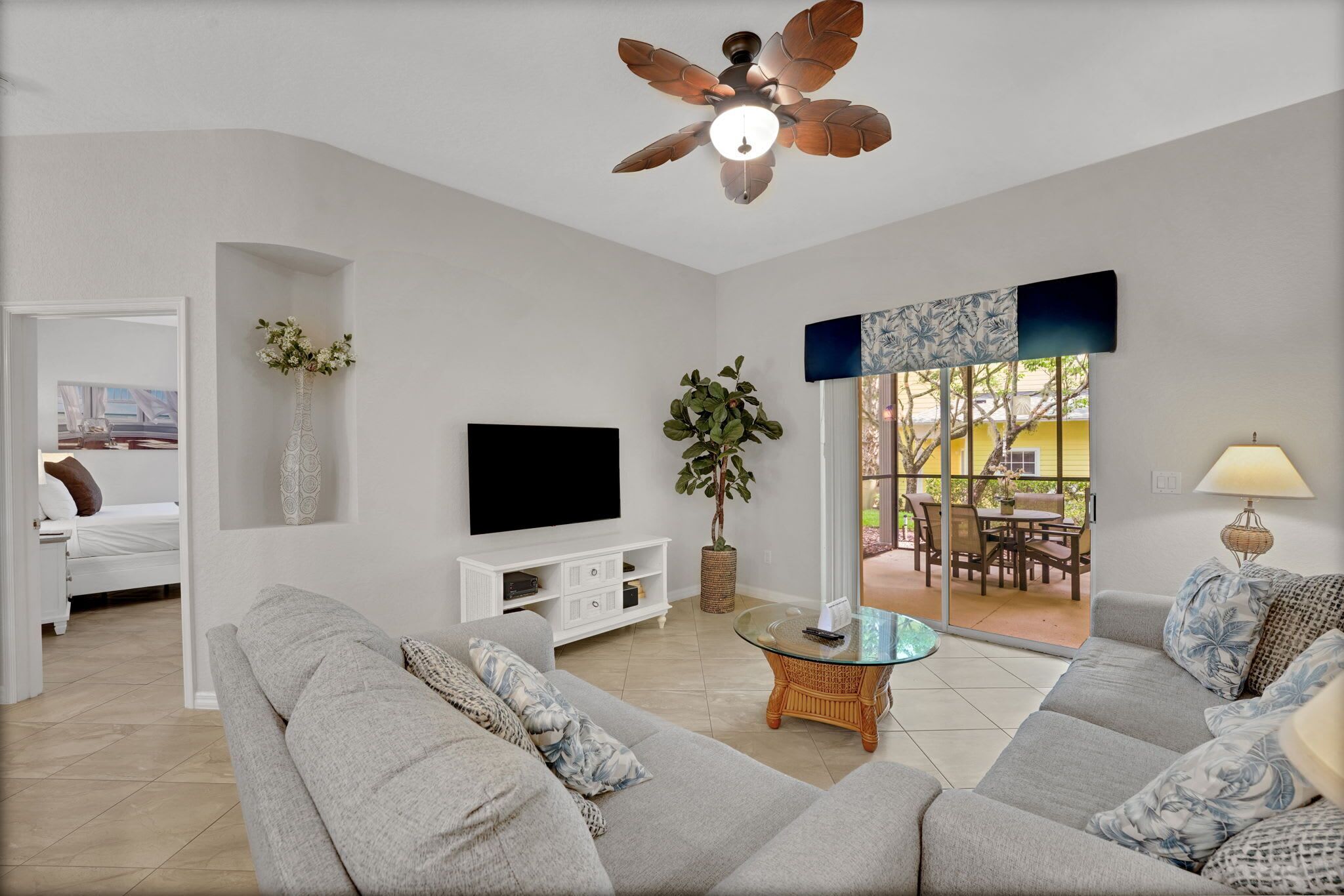 Ein modernes Wohnzimmer mit Deckenventilator, Flachbildfernseher, Zimmerpflanze, Couchtisch aus Weidengeflecht und einer Couch.
