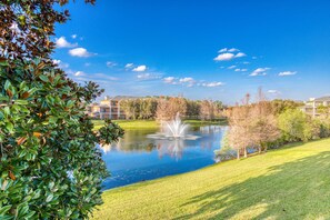 Ein friedlicher Park mit Teich, Springbrunnen und Gebäuden im Hintergrund.
