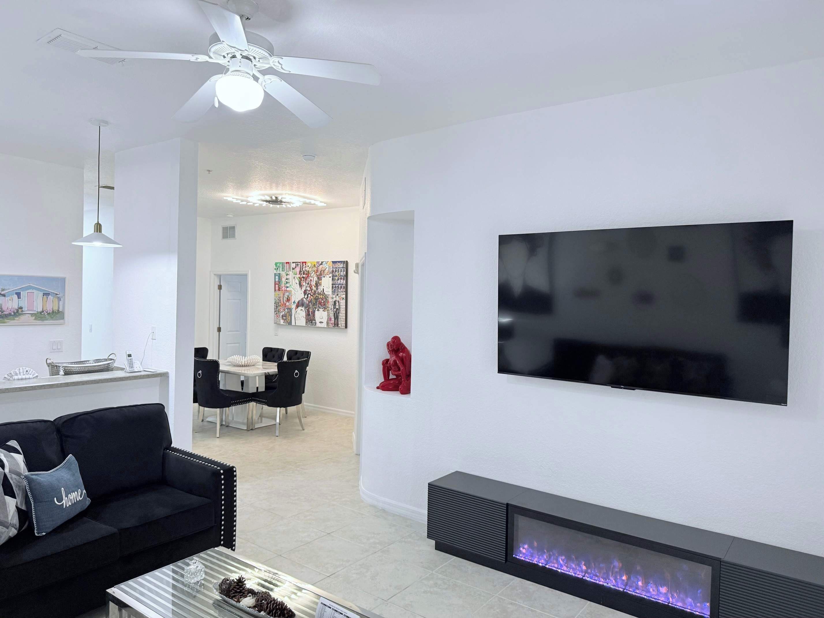 Een moderne woonkamer met een flatscreen televisie, een open haard, een plafondventilator en een eethoek.